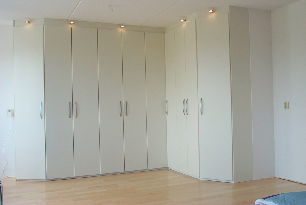 A corner wardrobe with angled end storage modules. The corner wardrobe has lights integrated at ceiling level for both aesthetic reasons as well as to provide a bit of extra light in the darker areas inside the wardrobe. Assembled by Flat Pack Happy.